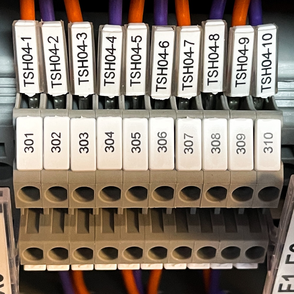 Close-up of a terminal block with labelled connections and wires, illustrating best practices for marking electrical panels and components. Labels include TSH04-1 to TSH04-10 above, numbers 301 to 310 below, with orange and purple wires attached.